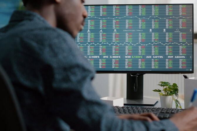 A professional working on cybersecurity in the financial sector, following SEC cybersecurity guidance. The person is seated in front of a large monitor displaying a complex array of stock market analytics and data encryption measures. This workspace exemplifies a secure environment for monitoring and protecting sensitive financial data against cyber threats, in compliance with regulatory standards for security and confidentiality in the stock exchange market.