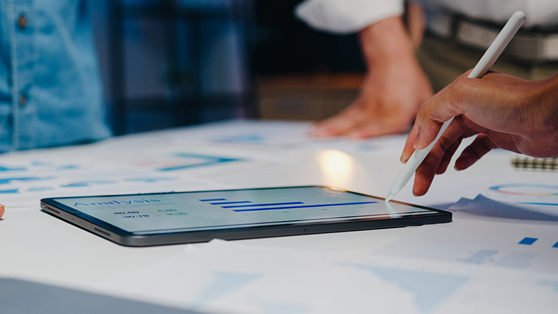 A hand holding a stylus going over an analysis of e-rate funding and technology goals.