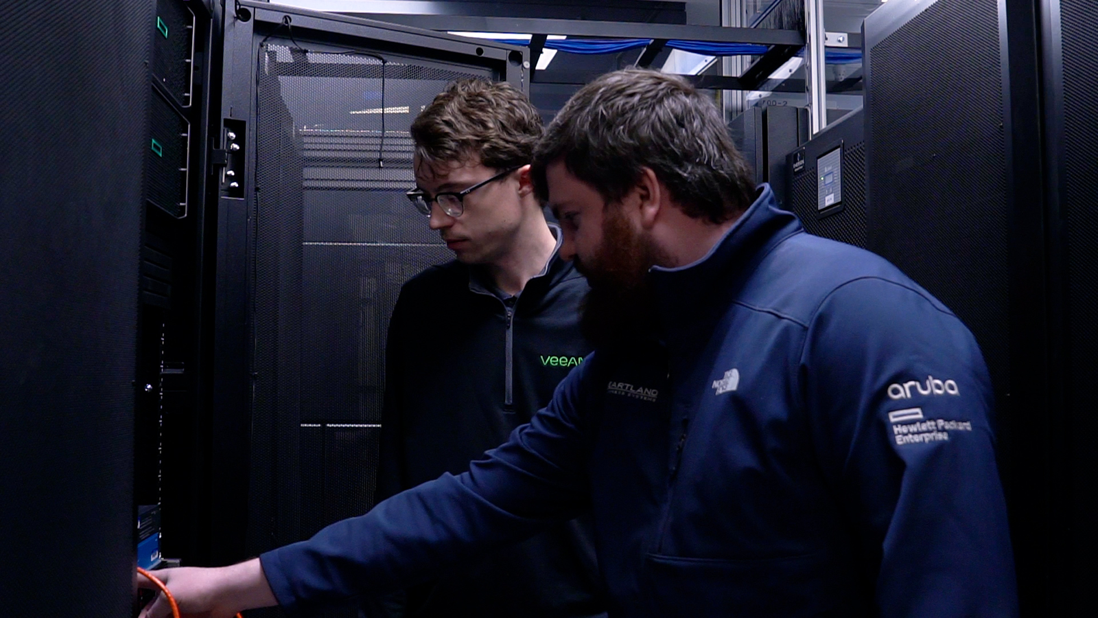 Two IT professionals examining and adjusting cables within a server rack in a data center.