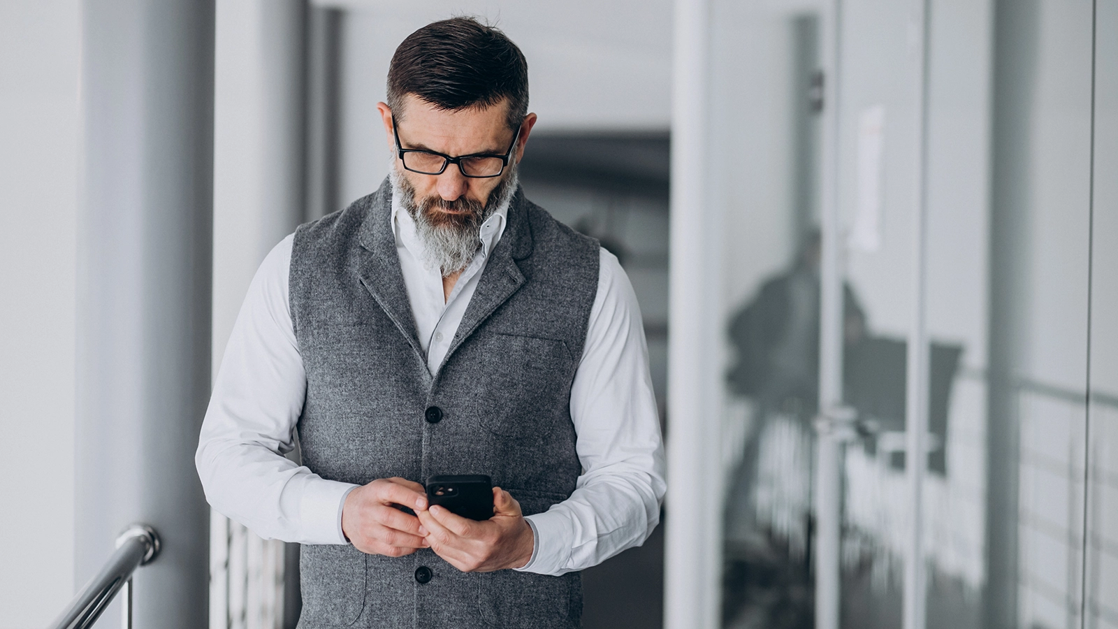 A bearded man in business attire focuses on his smartphone, emphasizing mobile device security for professionals managing sensitive data on the go.