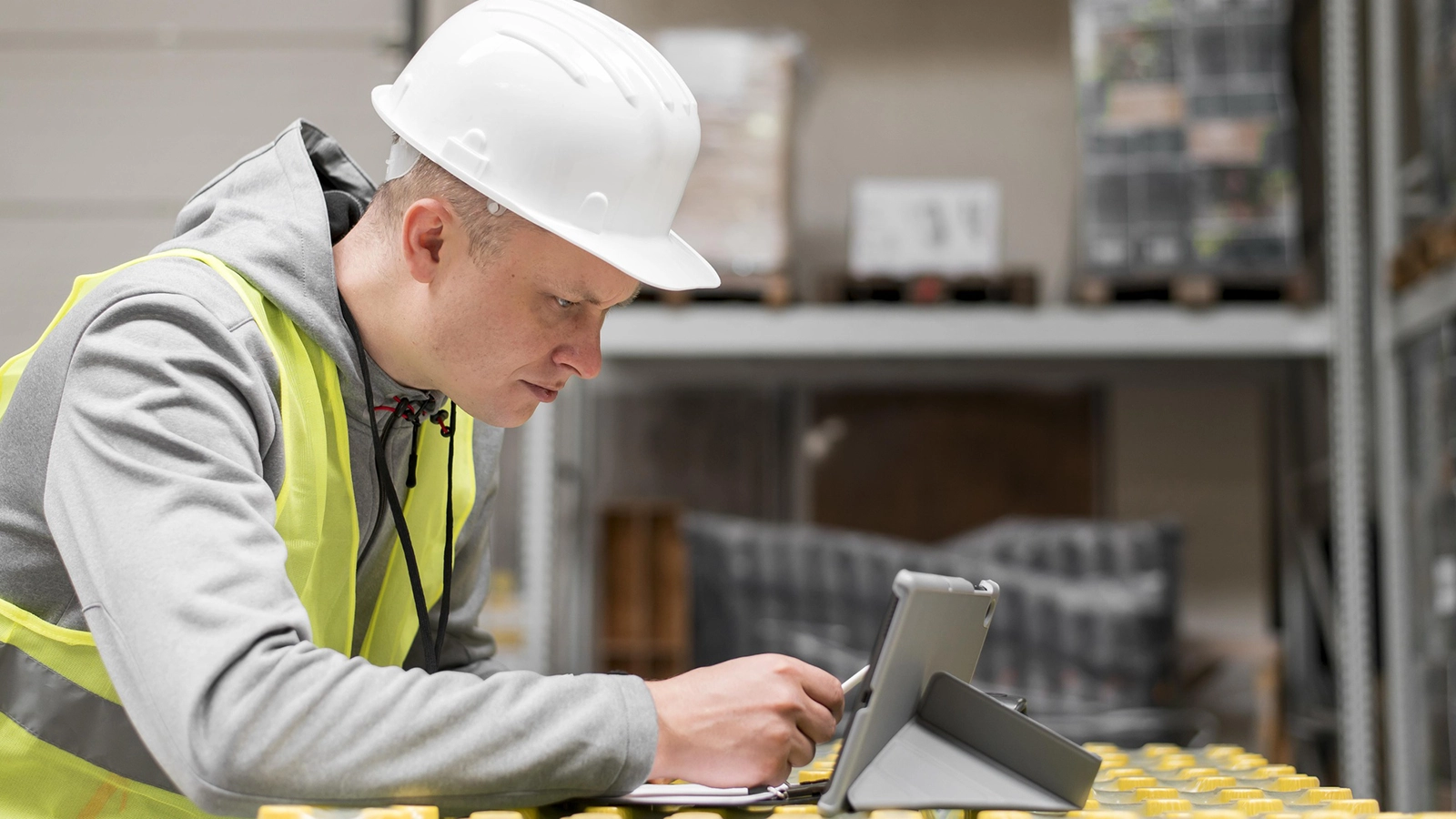 Worker in a warehouse wearing a hard hat and safety vest, using a tablet connected to a private cellular network for efficient task management.