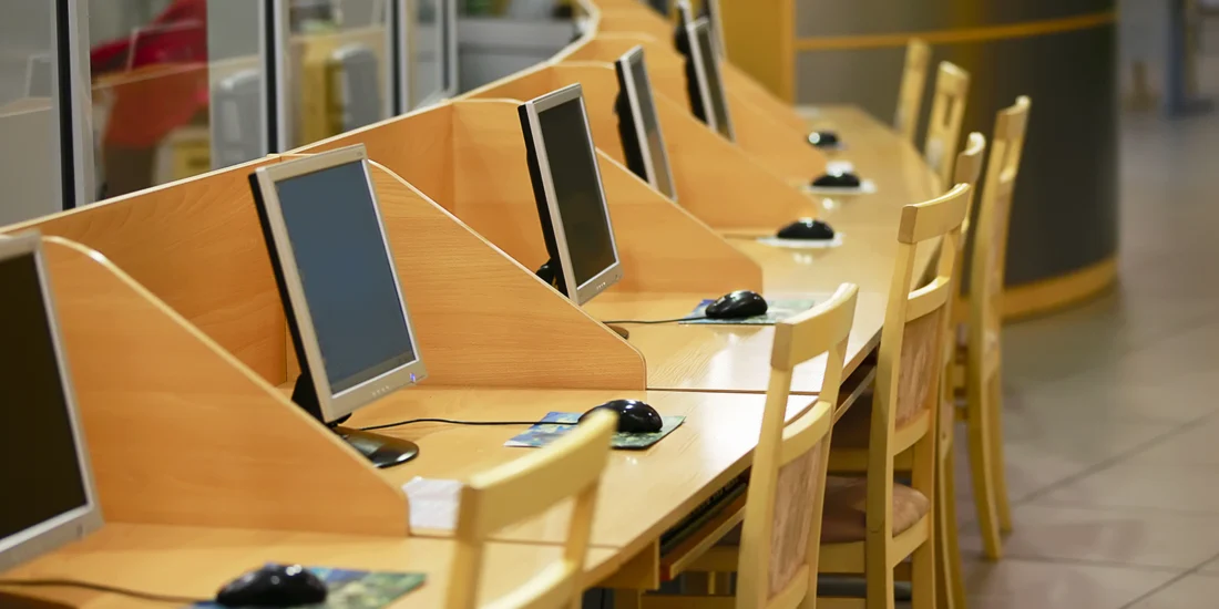 Computer monitors sit on wooden desks with a mouse and mouse pad, as well as wooden chairs.