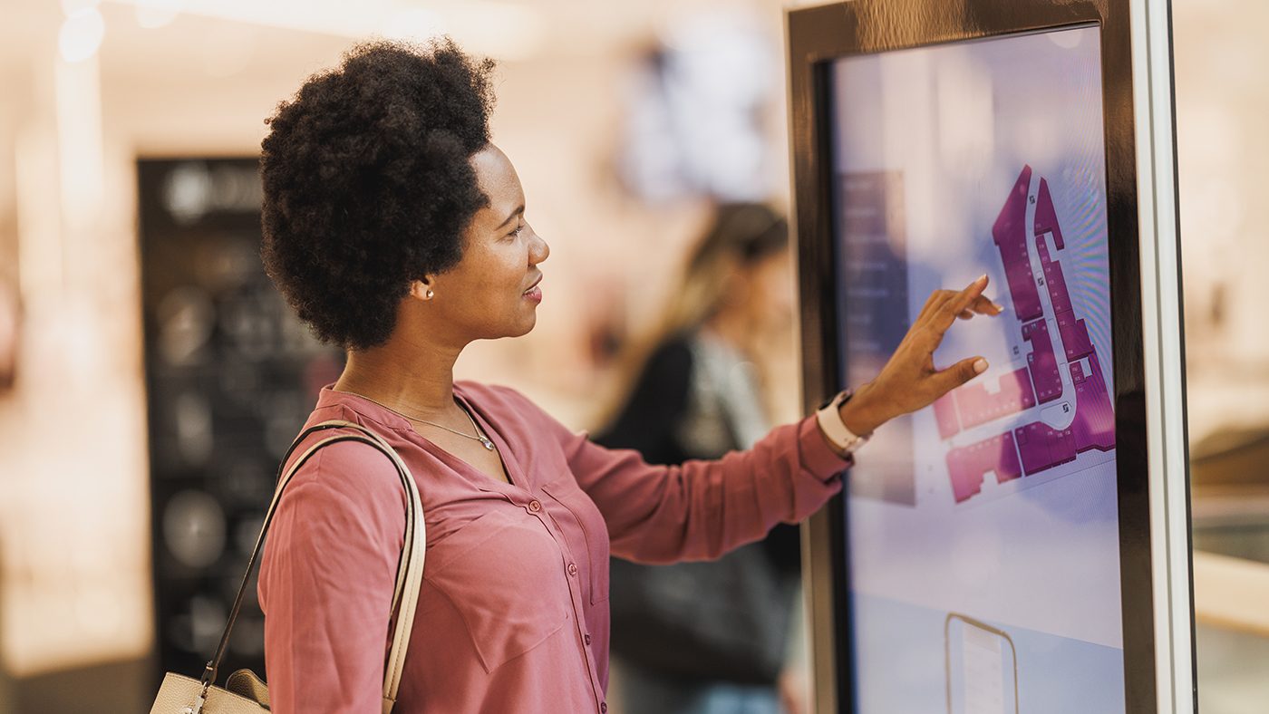 A shopper engages with an interactive digital signage kiosk, showcasing best practices in digital signage with its user-friendly interface and clear, vibrant graphics that enhance the customer experience in a modern retail setting.